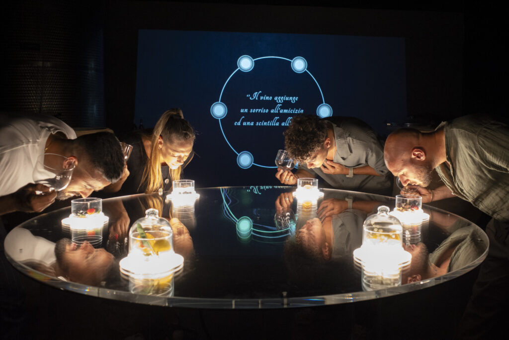 Guests leaning over a round lit table, holding glasses during an immersive wine tasting experience