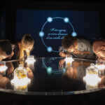 Guests leaning over a round lit table, holding glasses during an immersive wine tasting experience