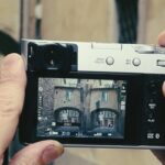 Image 1 — Hands holding a Fujifilm camera in multiple exposure mode framing a Florence archway during a double exposure photography Florence photo walk