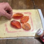 Hands positioning autumn leaves on the gel plate during an art workshop for kids Florence at Fatacadabra