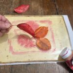 Layering red and orange leaves on the gel plate at a monoprint workshop Florence for children