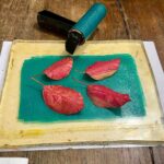 Teal acrylic color with red leaves on the gel plate at a creative workshop for kids Florence