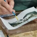 Lifting a Polaroid emulsion from its backing with a brush in warm water at a Polaroid emulsion lift Florence workshop