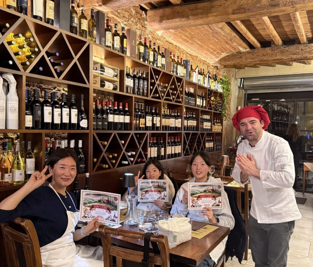 Students holding certificates with chef in wine cellar kitchen