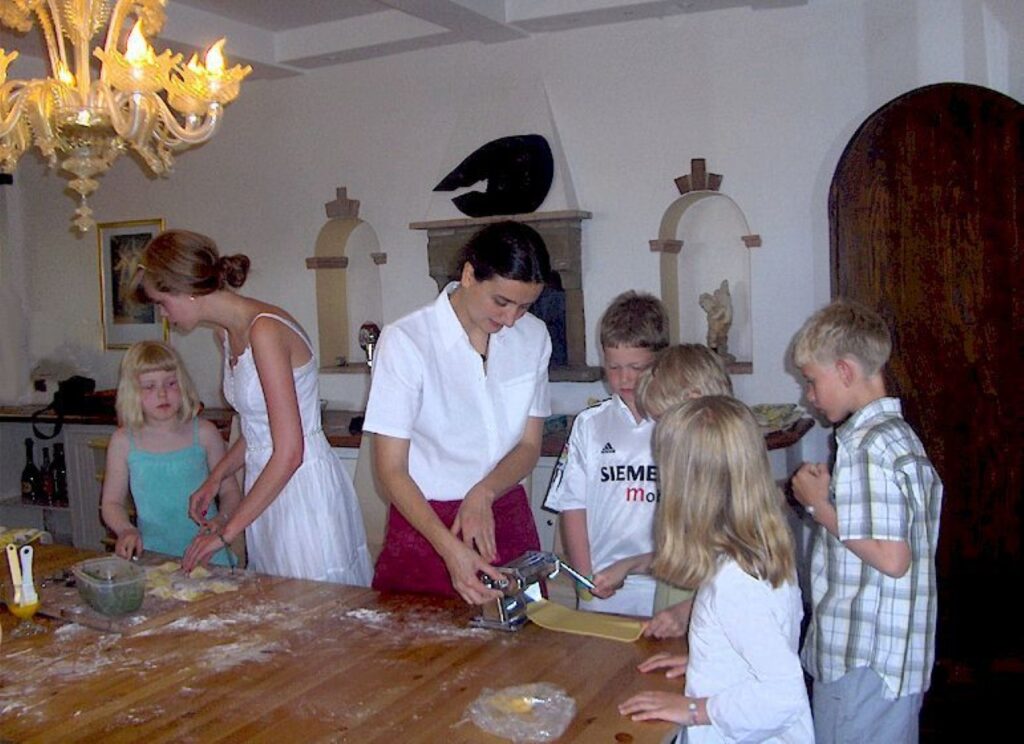 Children and adults making fresh pasta together during a family friendly Tuscan cooking class in a farmhouse.