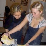 Two guests rolling and cutting pasta dough with a pasta machine in a Florence cooking class.