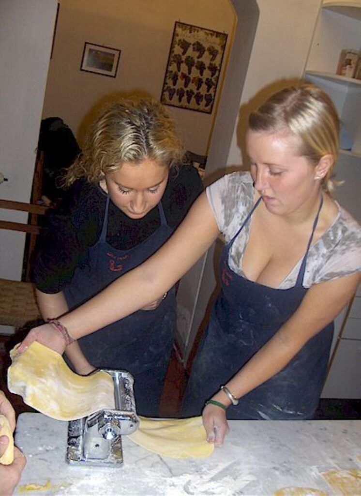 Two guests rolling and cutting pasta dough with a pasta machine in a Florence cooking class.