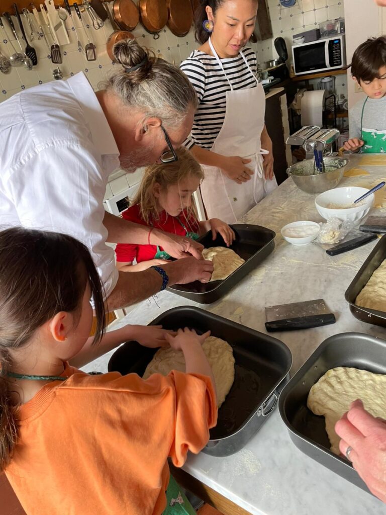 Children shaping dough with chef guidance during a family-friendly cooking class in Florence.