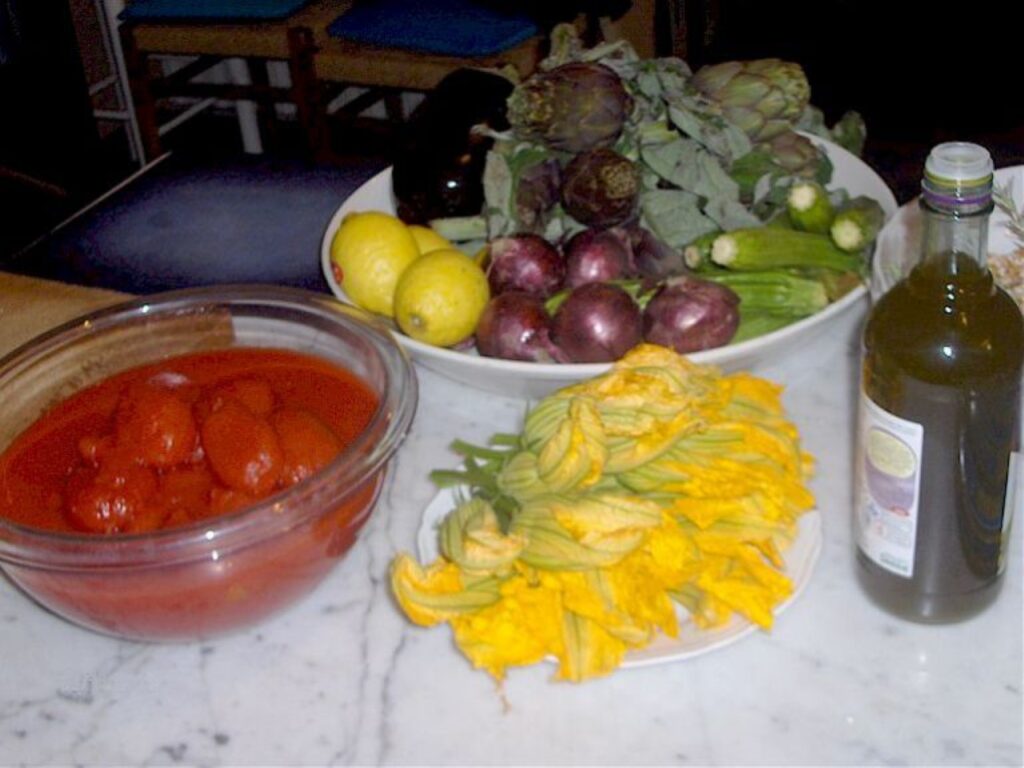 Fresh Tuscan vegetables, lemons, edible flowers, and olive oil on a kitchen counter before class.