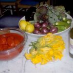 Fresh Tuscan vegetables, lemons, edible flowers, and olive oil on a kitchen counter before class.