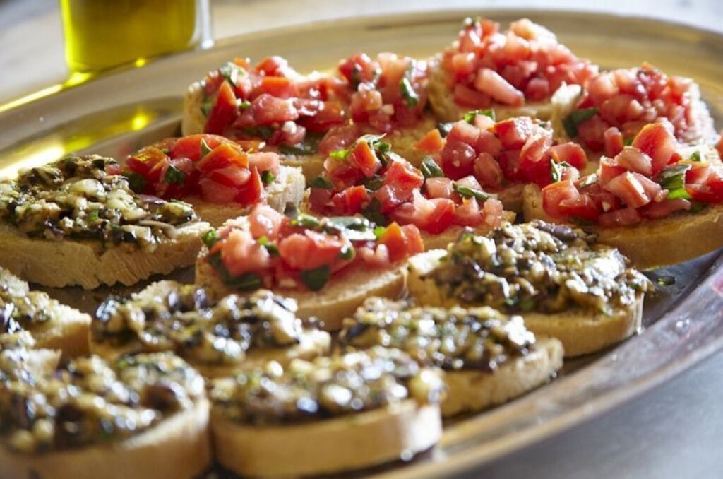 Plate of bruschetta topped with fresh tomato and savory spreads in a Tuscan cooking class.