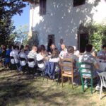 Large group dining in the farmhouse garden during a Tuscan countryside cooking class experience.