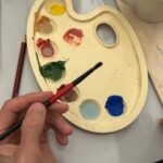 Participant mixing Maiolica colors on a palette during a ceramic painting in Florence