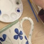 Student painting blue flowers on a ceramic mug during a ceramic painting in Florence