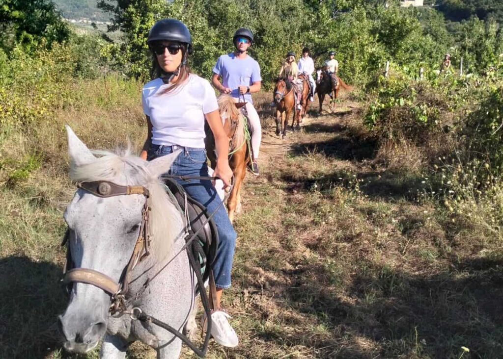 Group riding single file through a vineyard trail on the Chianti horseback lunch tour from Florence