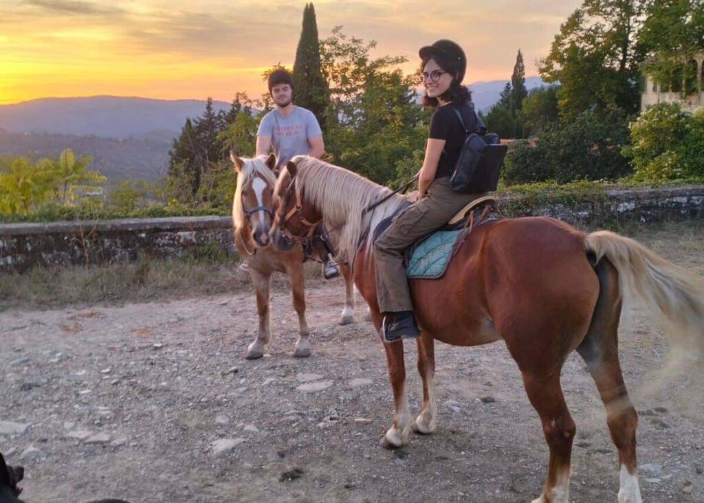 Two riders on horseback at a hilltop viewpoint at sunset during the Chianti horseback lunch tour from Florence