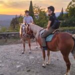 Two riders on horseback at a hilltop viewpoint at sunset during the Chianti horseback lunch tour from Florence