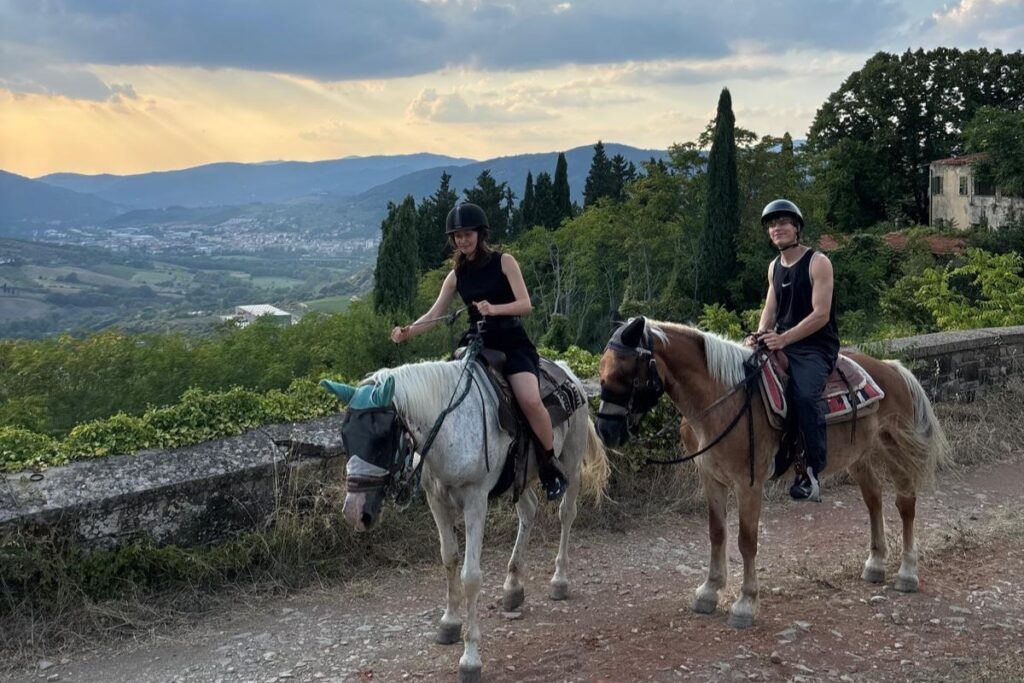 two riders on horseback at sunset overlooking Tuscan countryside