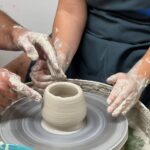 Shaping a vessel on the wheel during an intermediate pottery workshop Italy